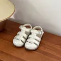 Close-up of white pearl finish baby girl walking sandals with closed-toe design - Beige