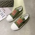 Macro view of green canvas sneakers featuring striped elastic bands and white toe caps. - 35 / Army Green