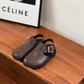 Detailed view of brown children's leather clogs with silver buckle on wooden bench - Brown
