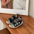 Close-up detail of black and white toddler sandals with soft soles on a wooden shelf - Black