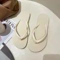 Detailed view of minimalist beige flip-flops on a textured neutral surface - Off White