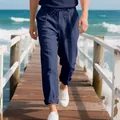 Detailed view of navy blue linen trousers worn by a man walking on a wooden beach pier - S / Bottoms / Navy Blue