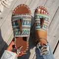 Detalle de sandalias planas bohemias con patrones geométricos y borlas de color marrón. - Verde claro