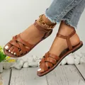 Close-up detail view of stylish brown flat roman sandals with an elegant cross strap design. - Brown