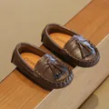 Nahaufnahme brauner Kinder-Loafer mit Lederstruktur und dekorativen Troddel-Details. - Dunkelbraun