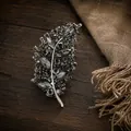 Vista macro de un elegante broche de hoja con cristales grises sobre un fondo madera rústica - Negro