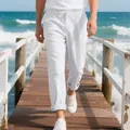 Close-up detail of men's loose white linen beach pants on a sunny ocean pier walkway - S / Bottoms / White