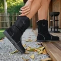 Close-up of black suede slouchy ankle boots with white stitching on outdoor deck. - Black