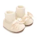Macro view of cream baby girl lace sock shoes featuring elegant ribbon bows and soft knit cuffs - Beige