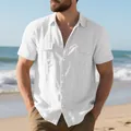Detail of a men's white linen short-sleeved shirt with double chest pockets on a beach. - White