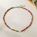 Close-up detail of colorful bead necklace featuring a gold letter D and white heart pendant charm - Letter D