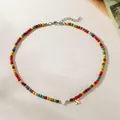 Close-up of a colorful beaded necklace with a gold letter X and white heart charm - Letter X