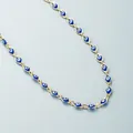 Nahaufnahme einer goldenen Halskette mit blauen Evil Eye Perlen auf grauem Grund - Blau