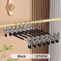 Close-up of black stainless steel pants hangers with clips on a golden closet rod. - Enhanced Version / Black