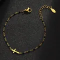 Nahaufnahme eines goldenen Armbands aus Edelstahl mit schwarzen Perlen und Kreuz-Anhänger - Gold Reinheit / Schwarz