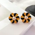 Détail macro de boucles d'oreilles fleurs en émail baroque avec une perle blanche - Noir
