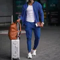 Ganzkörperansicht eines Mannes in einem blauen zweiteiligen Trainingsanzug mit Koffer - S / Oberteil Und Unterteil / Saphirblau