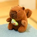 Adorable brown capybara plush toy doll holding a green avocado sitting on blue rug - Angel Capybara Avocado