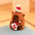 Adorable brown capybara plush toy wearing a Christmas hat and holding a mini snowman - Holding Christmas Snowman