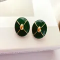 Macro shot of vintage dark green enamel stud earrings with gold cross pattern details. - Dark Green