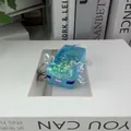 Détail d'un jouet anti-stress axolotl bleu à paillettes sur une surface de livre. - Axolotl Presse / Bleu Métallique