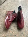 Close-up detail of burgundy faux leather ankle boots with double side zippers on stone floor - Red
