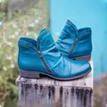 Detail view of teal leather ankle boots with side zippers on rustic wooden pedestal - 35 / Blue
