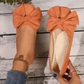 Dettaglio ravvicinato di eleganti ballerine scamosciate arancioni con grande fiocco decorativo su legno - 36 / Arancione