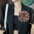 Detailopname van een 18 cm grote bruine stoffen camelia bloembloesem op een zwarte blazer. - koffiekleur