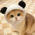 Close-up of a cute plush panda-themed hat worn by a ginger cat on a beige grid mat - Suitable for Cats and Dogs / Red Panda / Black and White