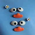 Detail view of funny cartoon big eyes and orange mouth shoe charms on blue surface - Emoji Flower Shoe Charm Kit / Set of 2