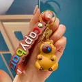 Close-up van een schattige capibara sleutelhanger met een kleurrijke polsband in de hand - Snotbel Stapelbare Capibara
