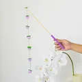 Mano che tiene una canna da pesca per gatti con palline di feltro viola e foglie verdi - Bacchetta Gatto Uva Viola / Viola