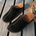 Close-up detail of black suede mules featuring white contrast stitching and chunky wood heels. - 36 / Black