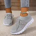 Detailed view of grey breathable fly-knit sneakers with white sole on a model's feet. - 36 / Gray