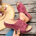 Close-up detail of burgundy wedge sandals with elegant floral laser-cut patterns on wooden deck. - Rose Red