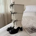 Primo piano di stivali alti neri e bianchi con fiocchi decorativi su letto bianco - 35 / Bianco