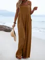 Model wearing a brown sleeveless wide-leg jumpsuit standing on a sandy summer beach. - S / Top And Bottom / Tan
