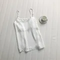 Detailed view of a white satin camisole with thin shoulder straps on a textured surface - M / Tops / White