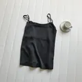 Close-up of a minimalist black satin spaghetti strap camisole laid on a white texture - M / Tops / Black