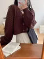 Primo piano della trama del cardigan marrone a trecce e dei bottoni in un contesto casual. - Taglia unica / Top / Caffè