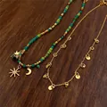 Primo piano di una collana bohémien vintage con ciondoli a luna e sole su sfondo legno. - Gold and Green (2-Piece Set)