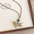 Close-up of a spotted puppy pendant necklace with a bow on a leather cord display - Khaki