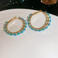 Close-up of gold hoop earrings featuring sparkling blue zircon stones on a white plate. - Sky Blue