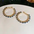 Detailed view of gold hoop earrings featuring elegant dark blue cubic zirconia stones. - Blue
