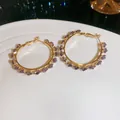 Elegant gold hoop earrings featuring sparkling faceted purple zircon crystals on a white plate - Purple