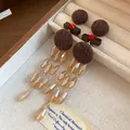 Vista detallada de pendientes de madera vintage con bolas de lana marrón y flecos - Poste de plata para pendientes - Café