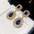Macro detail of vintage palace style gold earrings with blue water drop crystals - Silver Earring Post - Gold - Blue