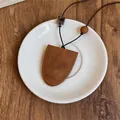 Detail van een vintage bruine lederen hanger ketting op een wit porseleinen bord - Zadelsteek Geometrische Stijl (Ketting 3)