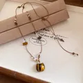 Détail d'un collier pendentif chat rétro avec œil de tigre et cordon en cuir perlé. - Marron